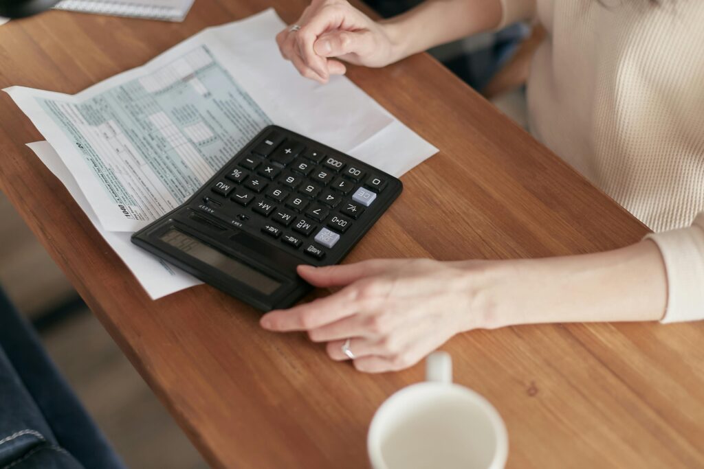 pexels-photo-6963030-6963030 Focused individual using calculator to manage personal finances at wooden desk.